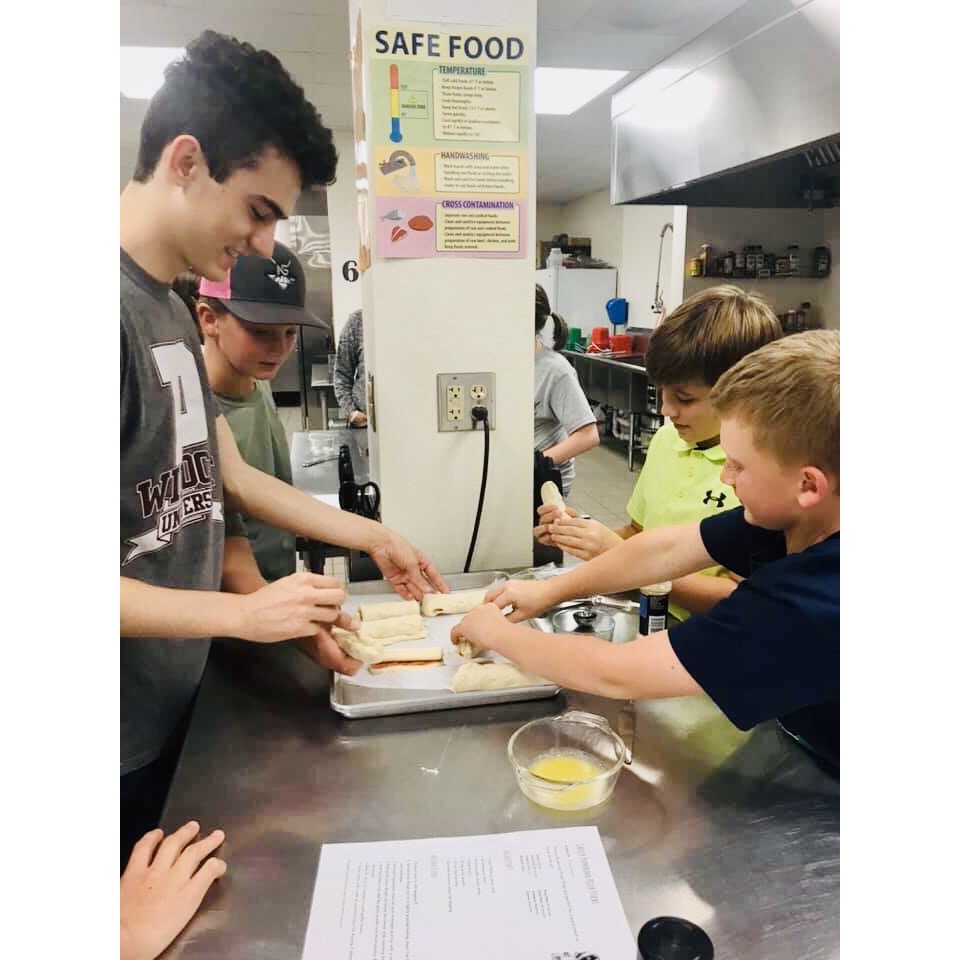 4-H members rolling together crescent roll dough, pepperoni's and mozzarella cheese sticks.