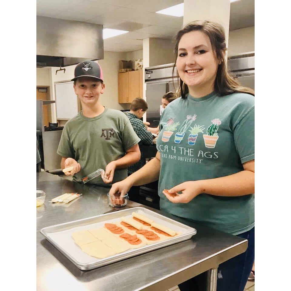 4-H members placing mozzarella cheese sticks on crescent roll dough and pepperoni's.